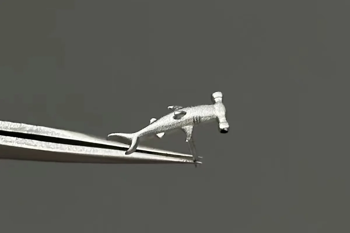 Sterling silver hammerhead shark earring held by tweezers, showing the textured hammer-shaped head and curved tail