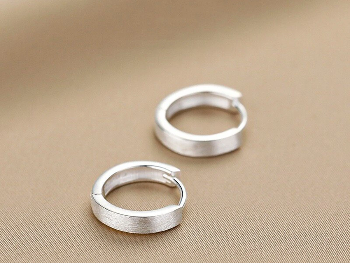 Pair of pure silver huggie hoop earrings with brushed finish lying on neutral fabric
